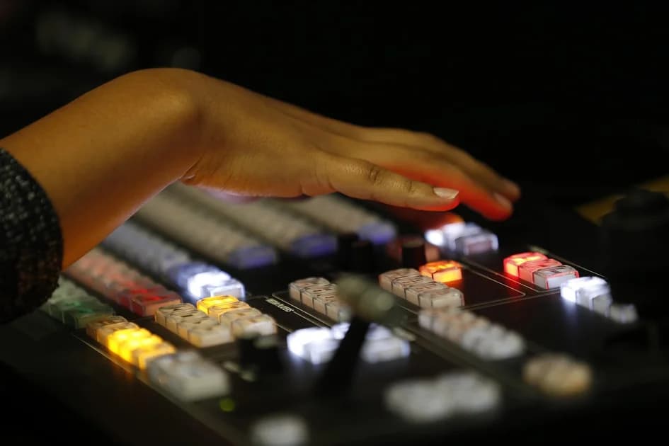 A hand over the lit buttons of a live video production switcher